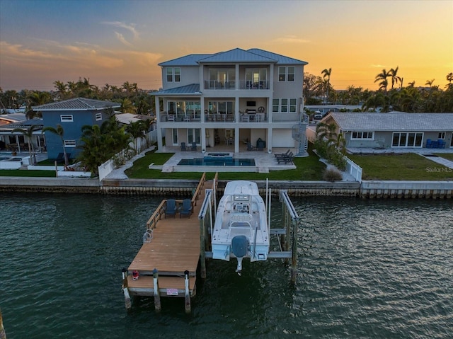 back of property at dusk featuring a patio area, a water view, a balcony, and a fenced backyard