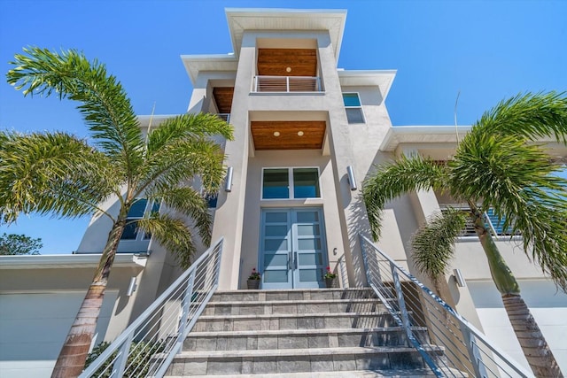 view of exterior entry with french doors, a balcony, and stucco siding