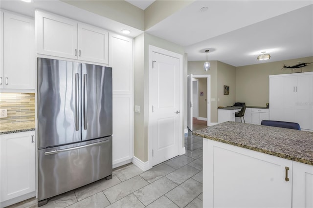 kitchen featuring stone counters, decorative backsplash, freestanding refrigerator, white cabinetry, and baseboards