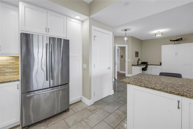 kitchen featuring decorative backsplash, freestanding refrigerator, white cabinetry, dark stone countertops, and baseboards