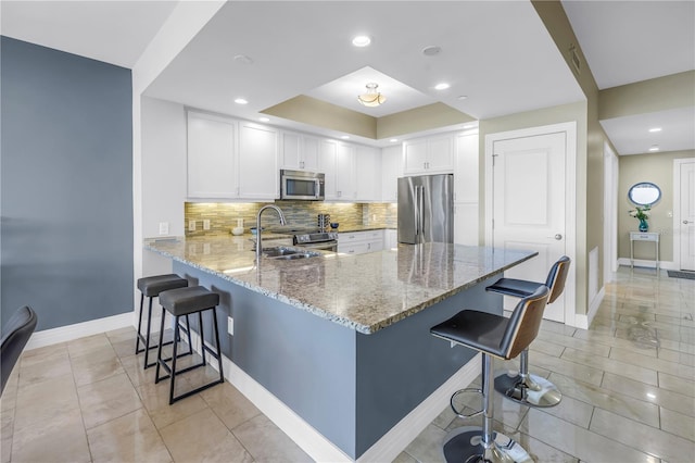 kitchen featuring light stone counters, stainless steel appliances, white cabinetry, a sink, and a peninsula