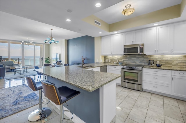 kitchen with decorative backsplash, appliances with stainless steel finishes, a peninsula, white cabinetry, and a sink