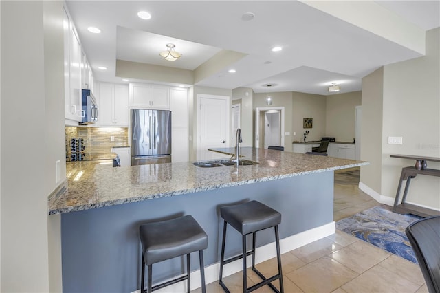 kitchen with light stone counters, stainless steel appliances, white cabinets, a sink, and a peninsula