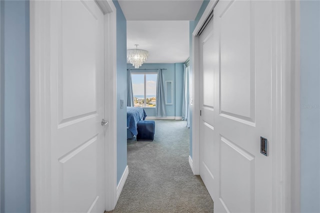 hall featuring carpet, a chandelier, and baseboards