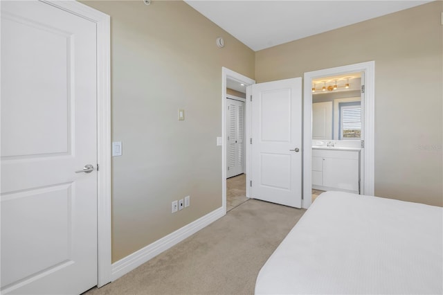 bedroom featuring baseboards, ensuite bathroom, a sink, and light colored carpet