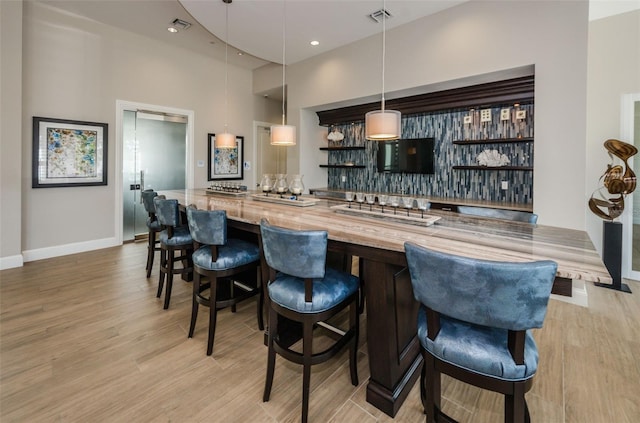 bar featuring baseboards, visible vents, hanging light fixtures, wet bar, and light wood-type flooring