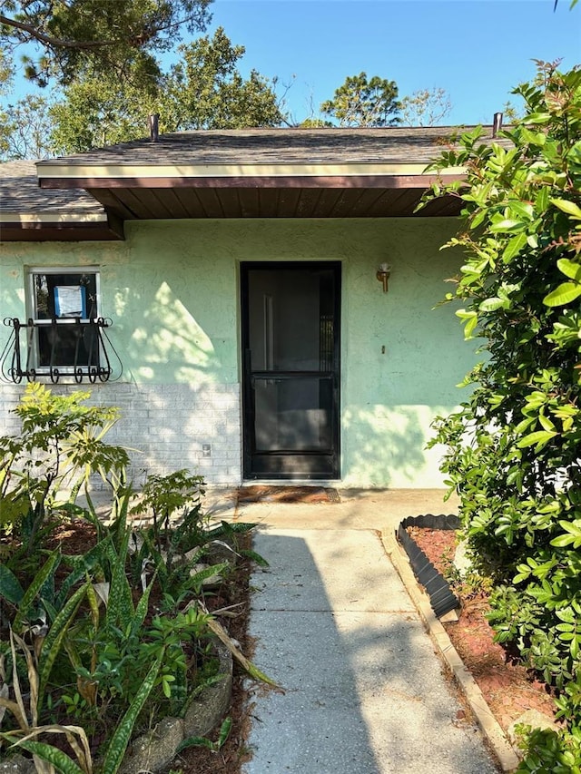 doorway to property with stucco siding and a shingled roof