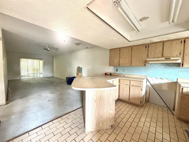 kitchen with under cabinet range hood, open floor plan, light brown cabinetry, light countertops, and a peninsula