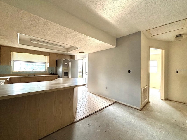 kitchen featuring stainless steel refrigerator with ice dispenser, a sink, a tray ceiling, a textured ceiling, and baseboards