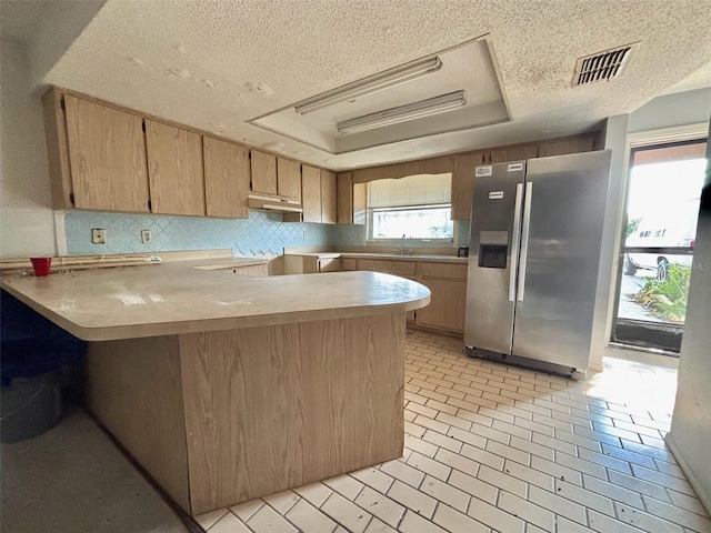 kitchen with visible vents, under cabinet range hood, a tray ceiling, stainless steel refrigerator with ice dispenser, and a sink