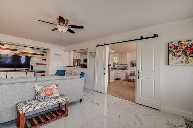 living area featuring marble finish floor, a barn door, ornamental molding, ceiling fan, and baseboards