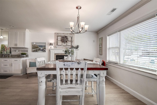 dining area featuring light wood-style floors, baseboards, visible vents, and crown molding