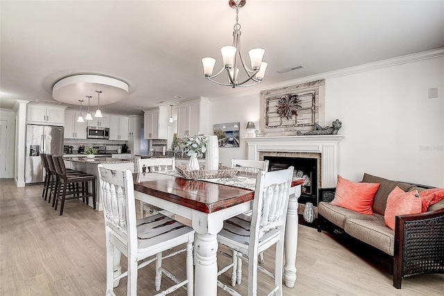 dining space featuring crown molding, light wood-style floors, visible vents, and a fireplace