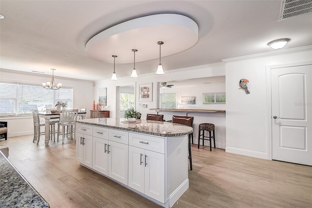 kitchen featuring light wood-style flooring, a kitchen island, visible vents, a kitchen breakfast bar, and white cabinets