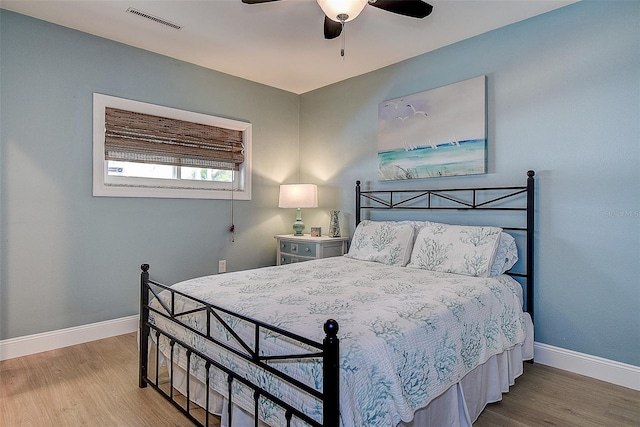 bedroom featuring a ceiling fan, visible vents, baseboards, and wood finished floors