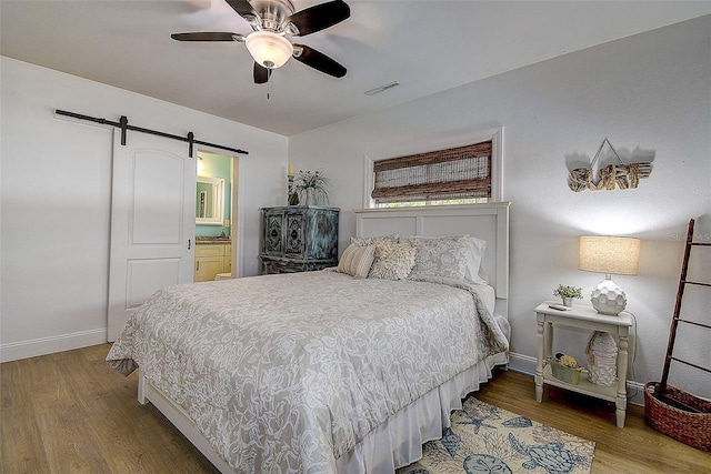 bedroom with baseboards, a barn door, visible vents, and wood finished floors