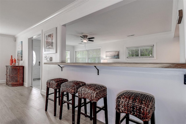 kitchen with light wood-type flooring, baseboards, a breakfast bar area, and crown molding