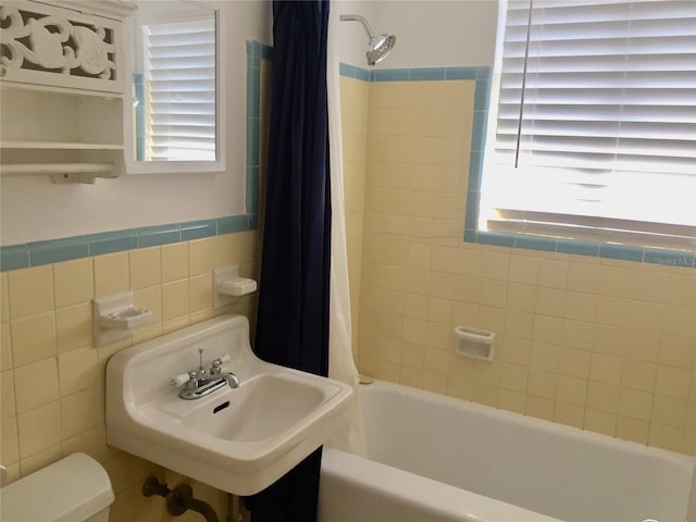 bathroom with a sink, shower / bath combo with shower curtain, wainscoting, tile walls, and toilet