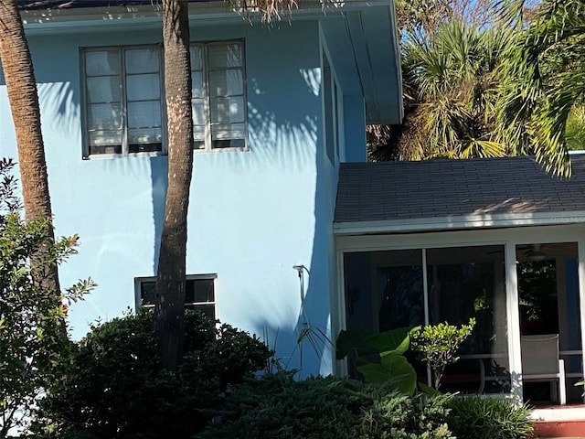 view of side of home with stucco siding, roof with shingles, and a sunroom