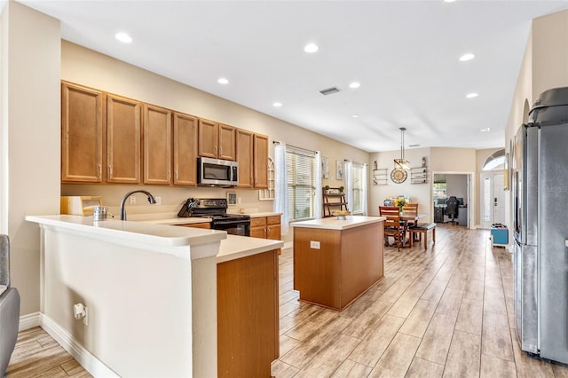 kitchen with a kitchen island, appliances with stainless steel finishes, brown cabinets, wood tiled floor, and light countertops