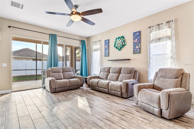 living room featuring light wood-style floors, a ceiling fan, visible vents, and a healthy amount of sunlight