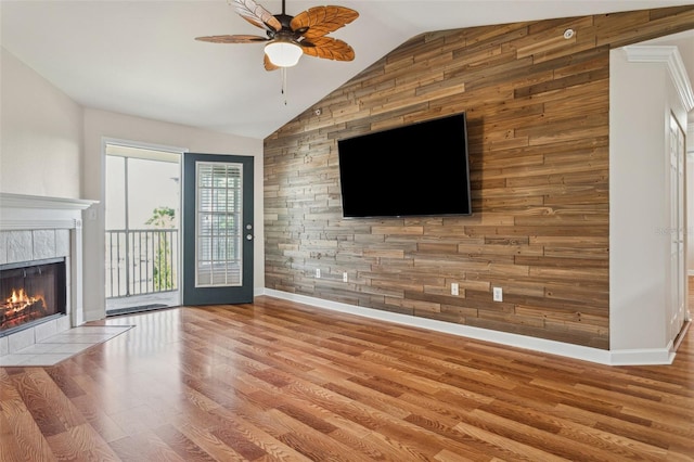 unfurnished living room with baseboards, a tiled fireplace, lofted ceiling, wood finished floors, and a ceiling fan