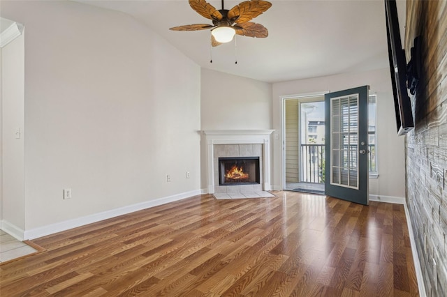 unfurnished living room with a tiled fireplace, baseboards, a ceiling fan, and wood finished floors