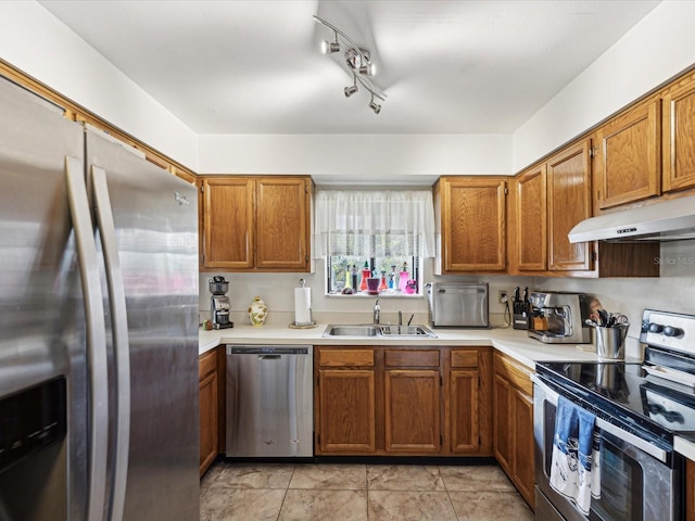 kitchen with brown cabinets, stainless steel appliances, light countertops, under cabinet range hood, and a sink