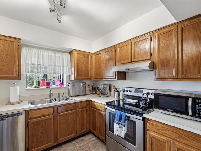 kitchen with appliances with stainless steel finishes, light countertops, a sink, and under cabinet range hood