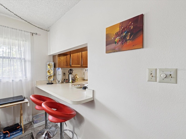 kitchen with light countertops, brown cabinetry, vaulted ceiling, a textured ceiling, and a kitchen breakfast bar