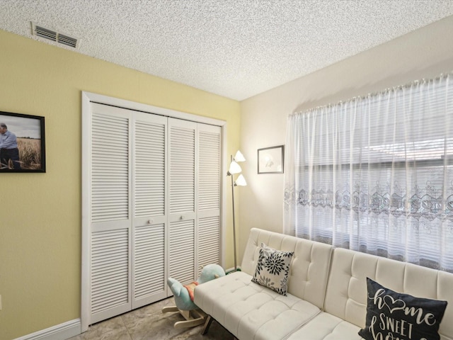 living area with a textured ceiling, visible vents, and baseboards