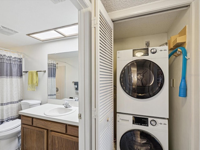 laundry room featuring a textured ceiling, laundry area, stacked washer / dryer, a sink, and visible vents