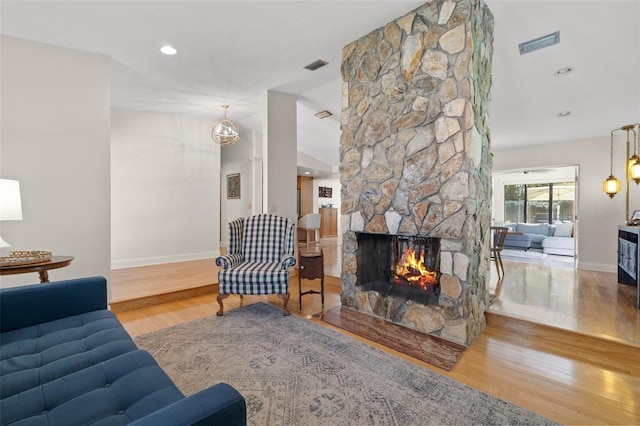 living room with visible vents, wood finished floors, and a stone fireplace