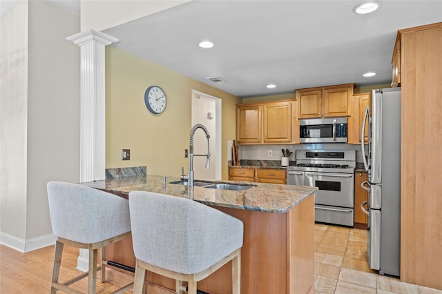 kitchen featuring visible vents, a peninsula, stainless steel appliances, stone counters, and a sink