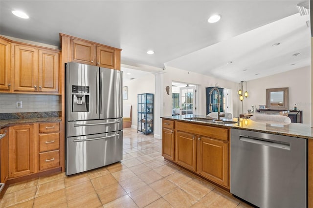 kitchen featuring a sink, appliances with stainless steel finishes, dark stone counters, tasteful backsplash, and ornate columns