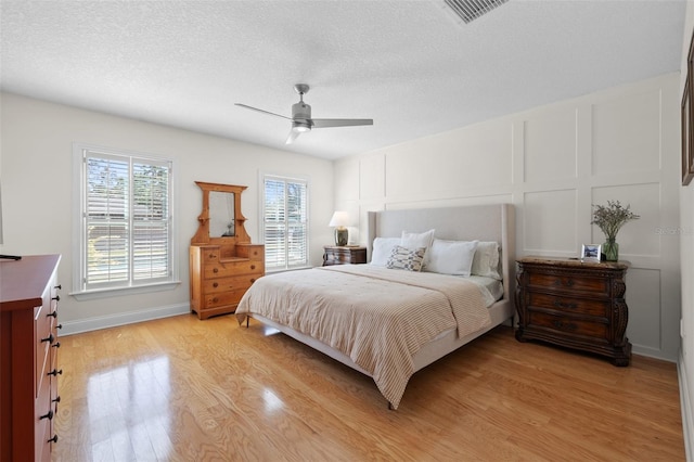 bedroom featuring visible vents, a decorative wall, a textured ceiling, and light wood finished floors