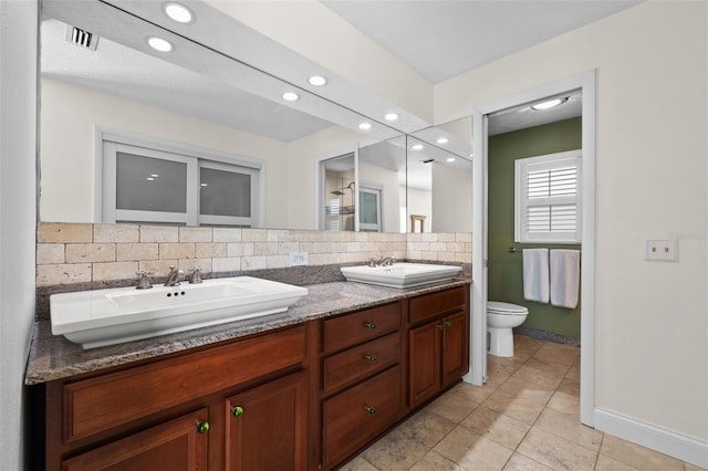 bathroom featuring double vanity, tasteful backsplash, a sink, and toilet