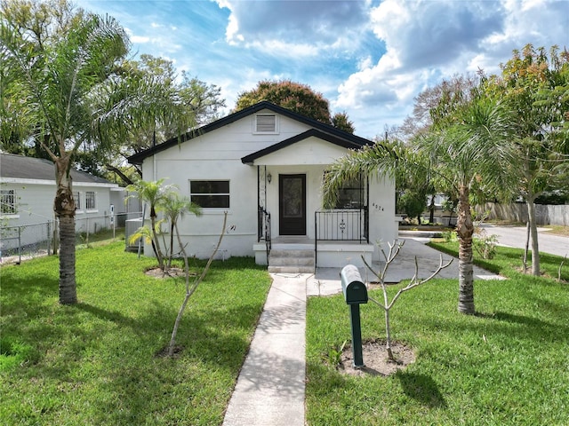 bungalow-style house with covered porch, a front lawn, fence, and stucco siding