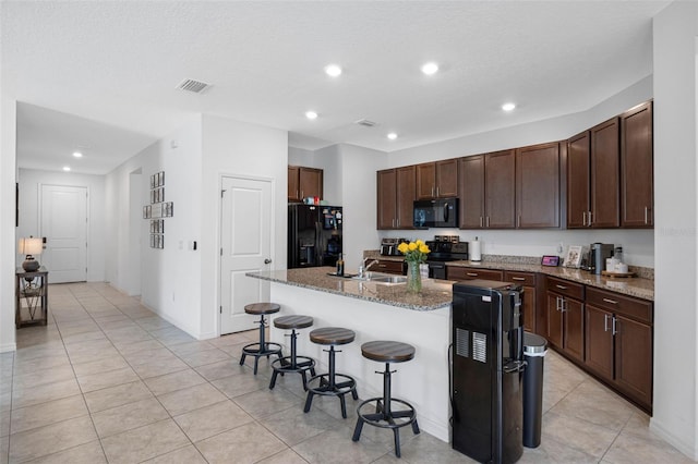 kitchen featuring a kitchen breakfast bar, a center island with sink, black appliances, and dark brown cabinets