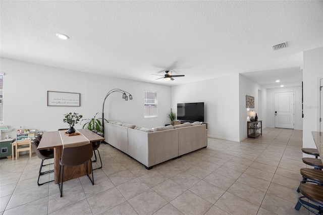 living room featuring light tile patterned floors, visible vents, a ceiling fan, stairs, and a textured ceiling