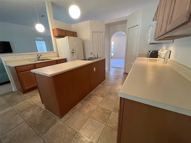 kitchen with arched walkways, a kitchen island with sink, white appliances, a sink, and light countertops