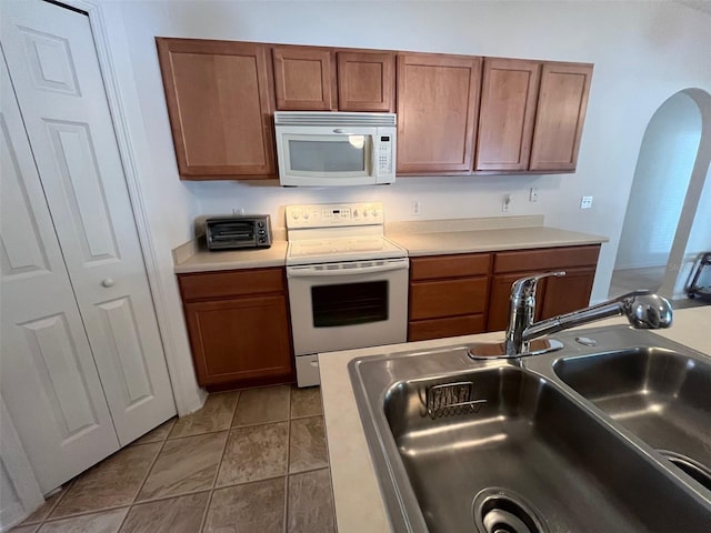 kitchen featuring white appliances, arched walkways, light countertops, and a sink