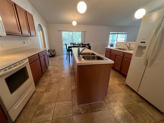 kitchen featuring a wealth of natural light, white appliances, a sink, and a kitchen island with sink