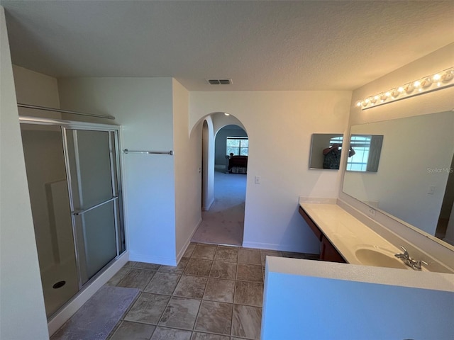 full bathroom with a textured ceiling, a shower with shower door, vanity, visible vents, and baseboards