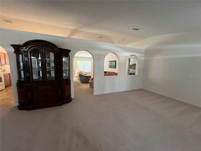 unfurnished room with light carpet, arched walkways, and visible vents