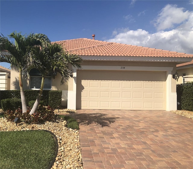 view of front of house featuring decorative driveway, an attached garage, a tile roof, and stucco siding