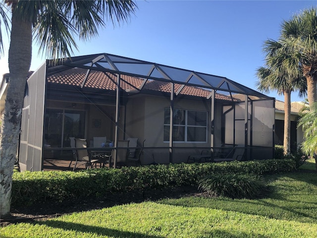 back of property with a lanai, a tiled roof, and a yard