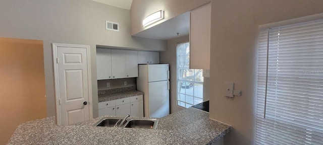 kitchen featuring a peninsula, a sink, visible vents, white cabinets, and freestanding refrigerator