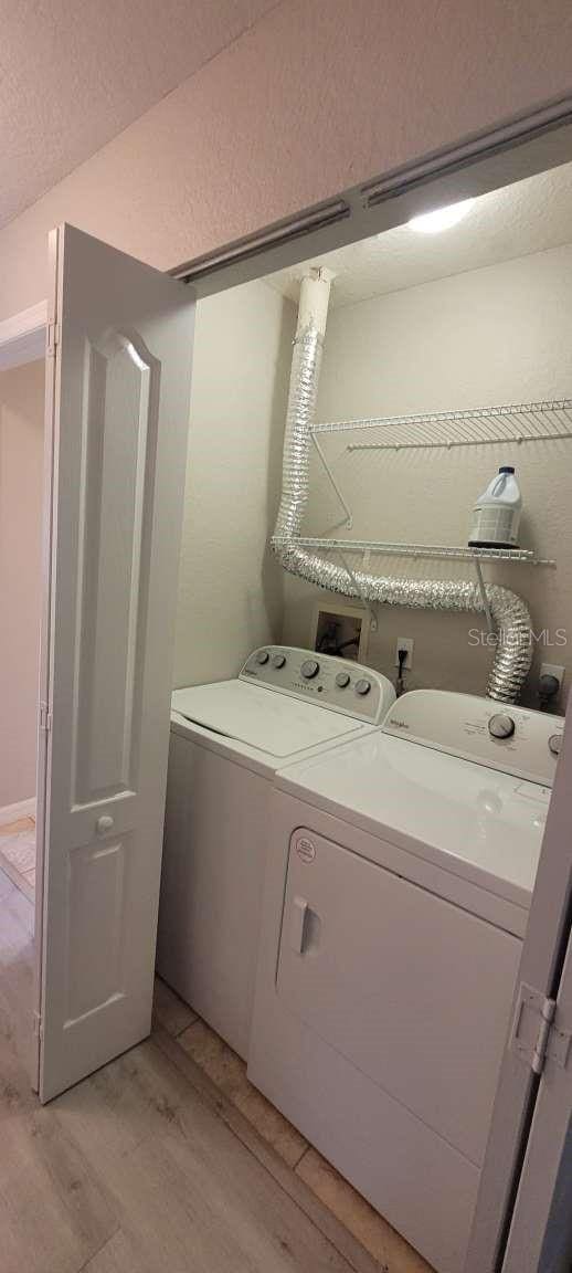 laundry room with a textured ceiling, laundry area, washer and clothes dryer, and light wood-style floors