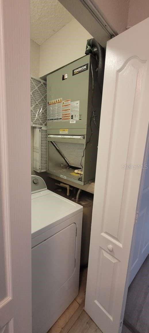 clothes washing area with heating unit, a textured ceiling, washer / dryer, light wood-type flooring, and laundry area